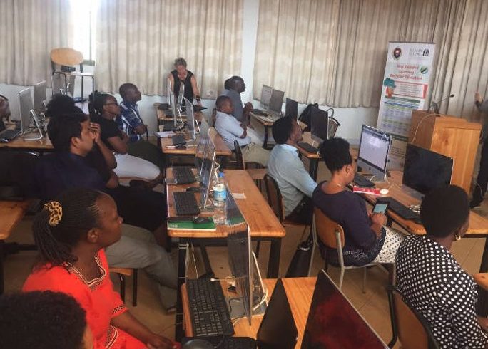 students sitting at a classroom behind their computers, listening to a presenter who is not visible on the photo